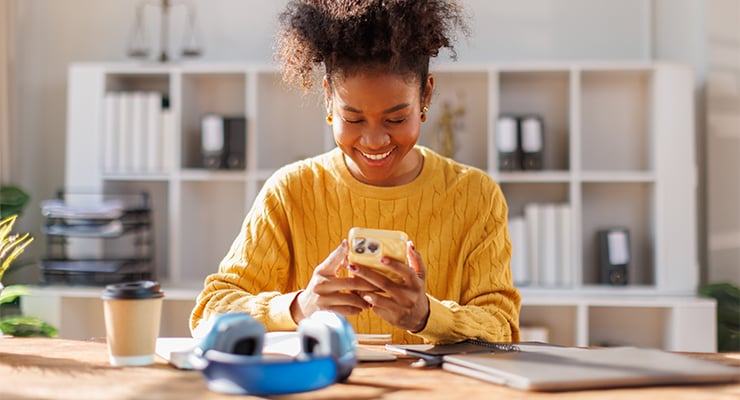 A woman wearing a yellow sweater and using her phone.