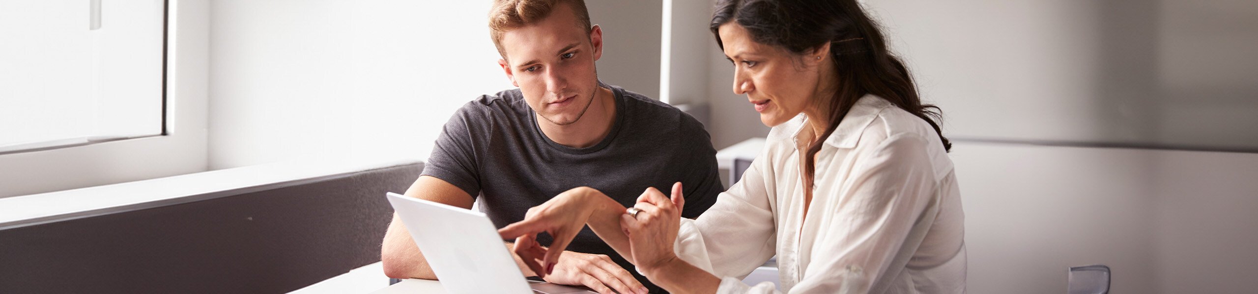 A young man and a woman looking and pointing at the screen of a laptop.