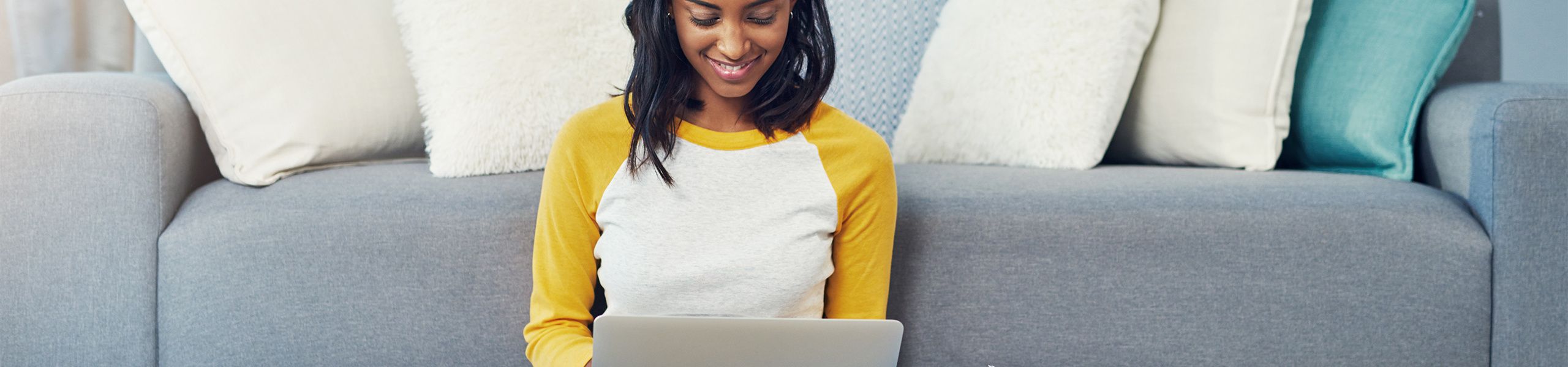 A student sitting by a couch and using her laptop.