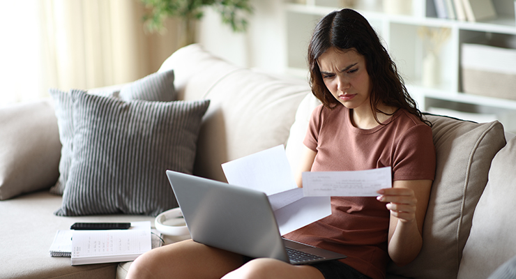 A student sitting on a couch at home while reviewing documents.
