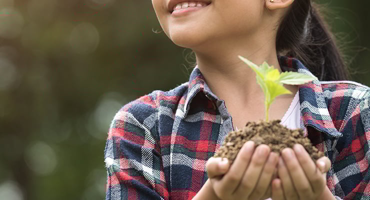 A student holding a plant and soil in her hands before planting.