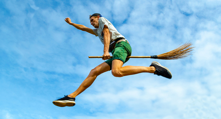 A man flying mid-air on a broom.