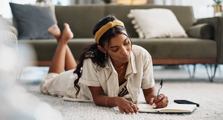 A student writing in a notebook on the floor.