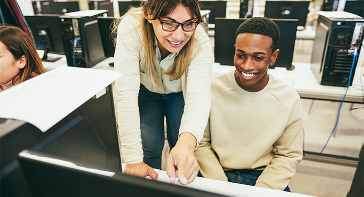 A professor helping a student on a computer during class.