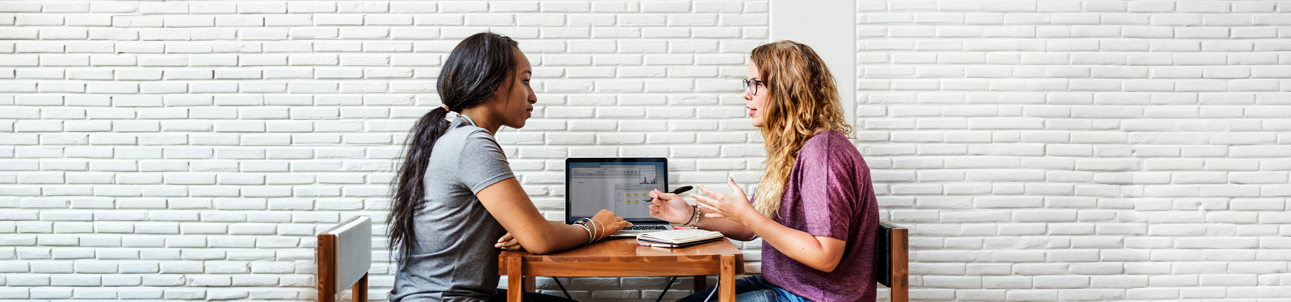 Two students sitting together at a table and collaborating on a project.