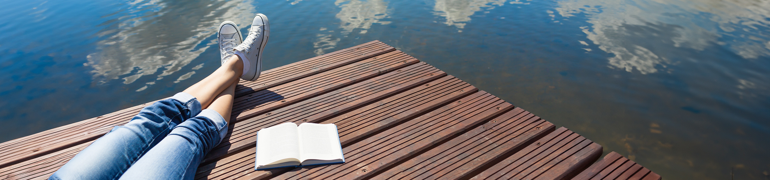 A person on a dock with a YA novel next to them.