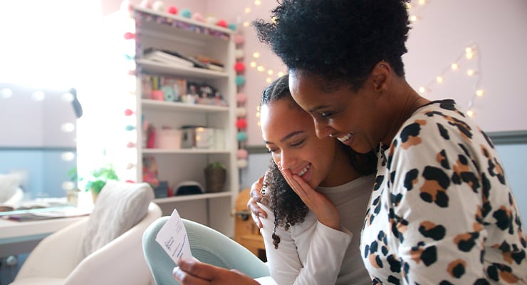 A mother hugging her daughter as they read a letter together.