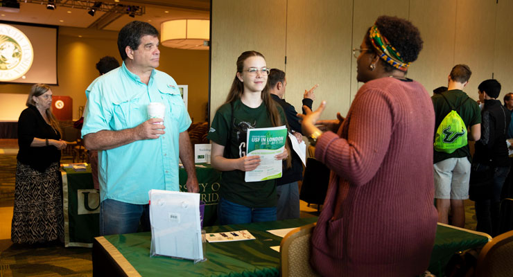 Student and parent talk to a USF representative at a college fair event.