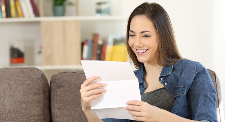 A high school student sitting on her couch at home reads her collage application response letter.