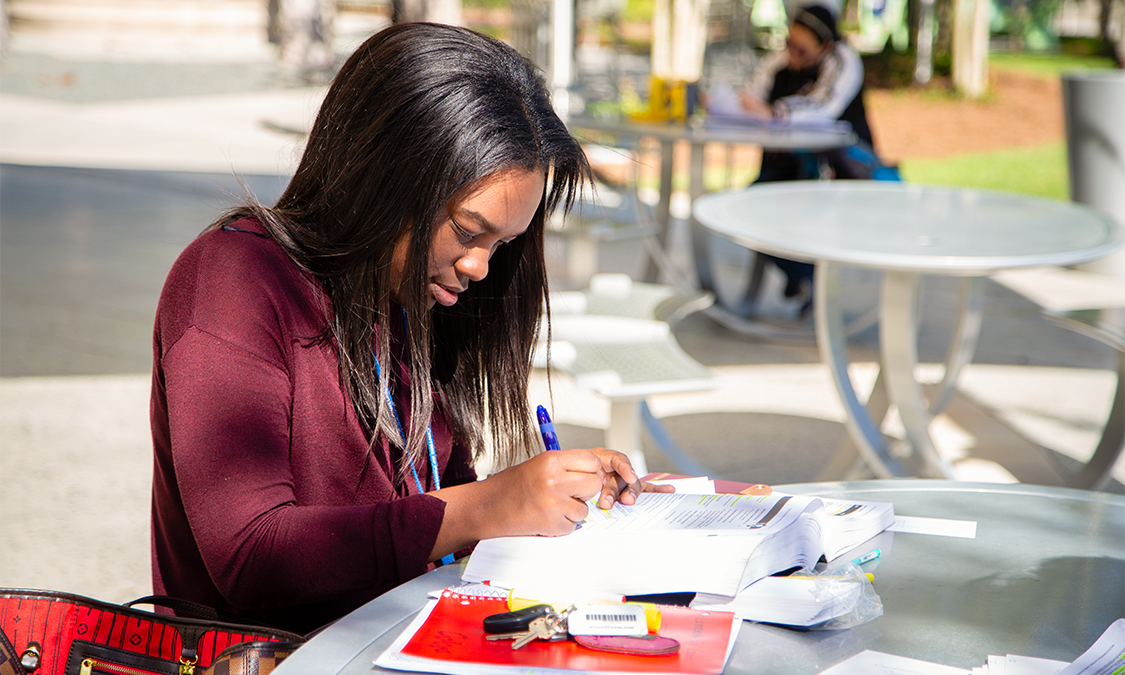 A female student sitting outside filling out scholarship paperwork