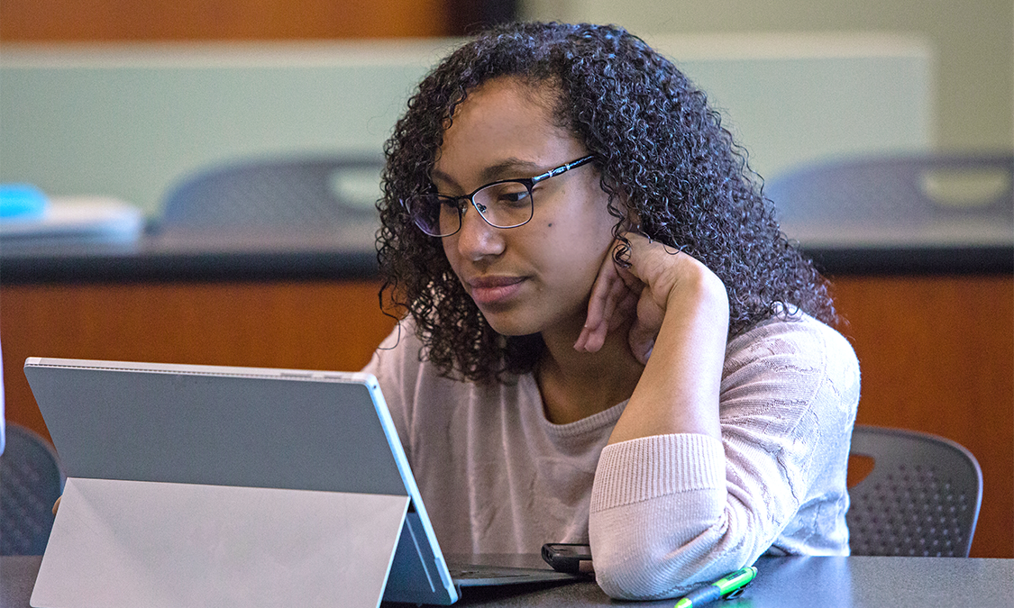 A student sitting in class using a tablet to take notes for college courses.