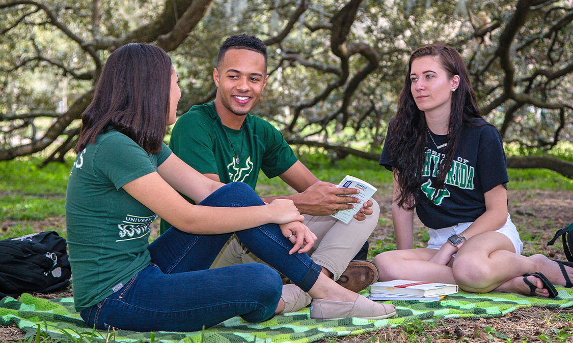 Three USF students sitting outside on-campus and having fun.